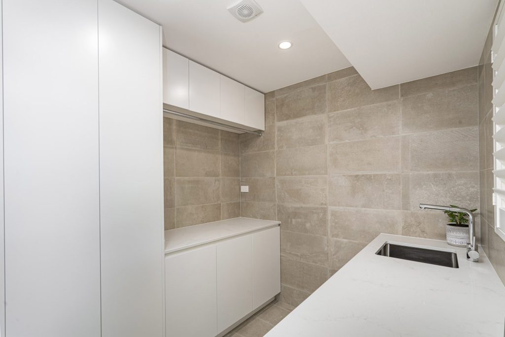 large format tiles in laundry with stone bench top and ample storage solutions in Castle Hill