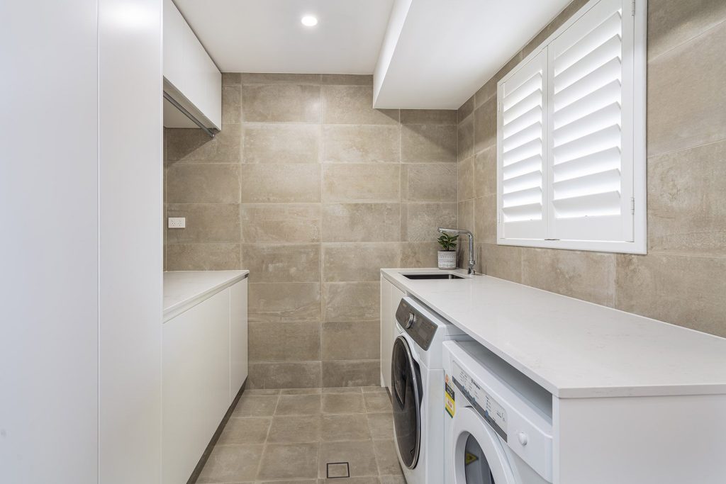 large format tiles in laundry with stone bench top and ample storage solutions in Castle Hill