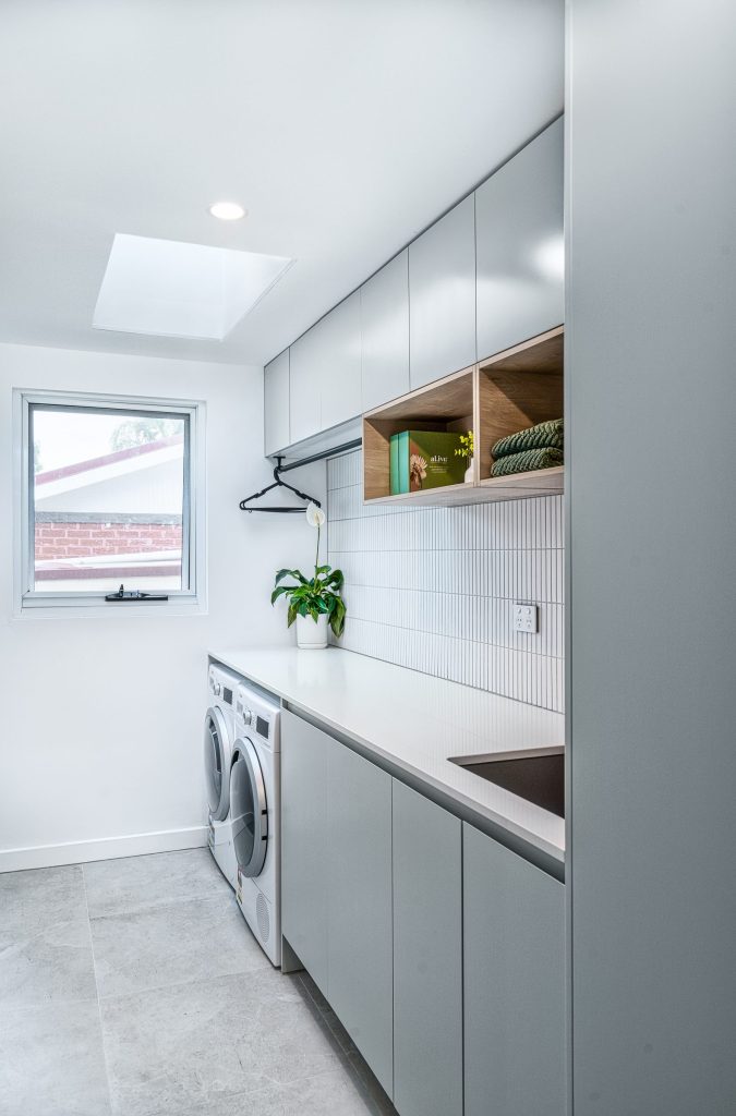 Custom-built laundry with quality cabinetry with stone bench top and tiled splashback