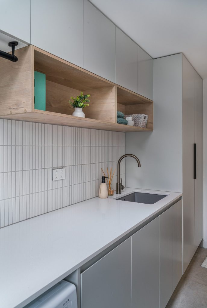 Custom-built laundry with quality cabinetry with stone bench top and tiled splashback and wooden custom shelves